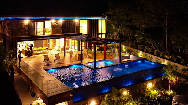 Una casa moderna con piscina, mobiliario exterior y un patio cubierto.