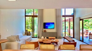 Un salón amplio con una televisión grande en la pared, un sofá, mesas de madera y sillas de mimbre.
