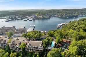 A coastal hotel with multiple buildings, a swimming pool, and a view of the sea and forested hills.