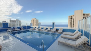 Una piscina en la azotea con sillones de descanso y vistas al océano y edificios.