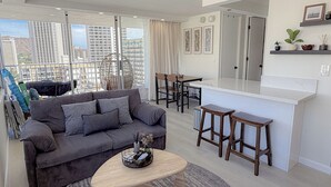 Una sala de estar moderna con un sofá gris, una mesa de centro de madera y un comedor con taburetes.