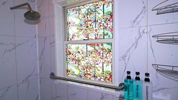 Casa de banho com chuveiro, uma janela de vitrais e produtos de higiene numa prateleira.