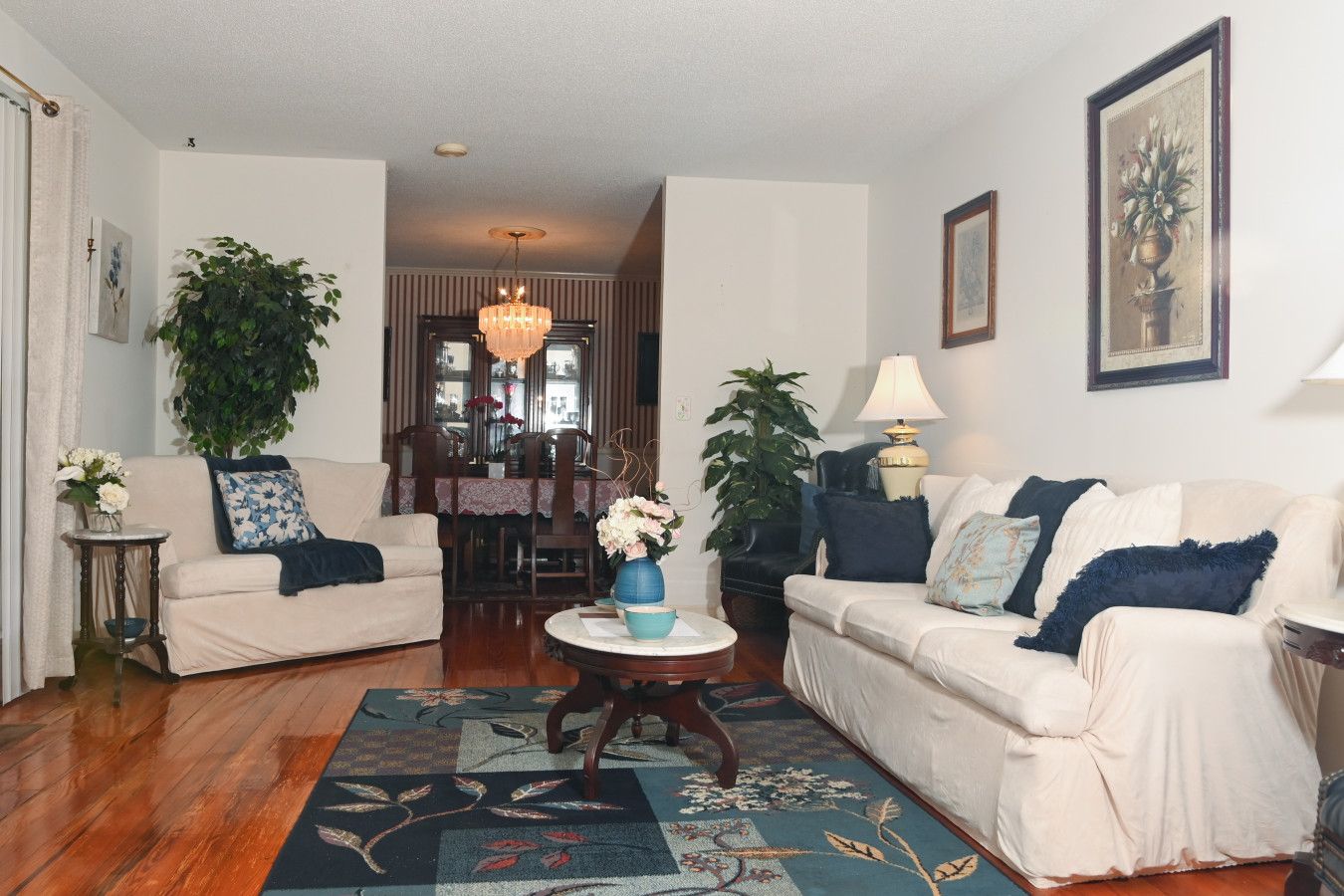 A living room with two sofas, a coffee table, a chandelier, and a dining area in the background.