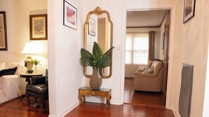 Un salon doté d’un parquet, d’un canapé, d’un fauteuil, d’une lampe, d’un vase, d’un miroir et d’une porte donnant sur une autre pièce.
