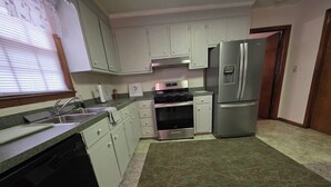 Une cuisine avec des meubles blancs, des appareils en acier inoxydable, un lave-vaisselle et un tapis à motifs.