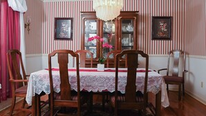 Une salle à manger avec une table dressée pour quatre personnes, entourée de chaises en bois, d’un lustre et d’une fenêtre agrémentée de rideaux.