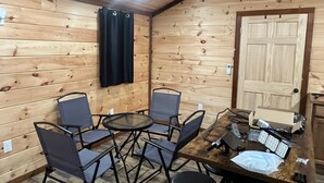 A wooden cabin interior with a dining table, four chairs, a small round table, and a door.