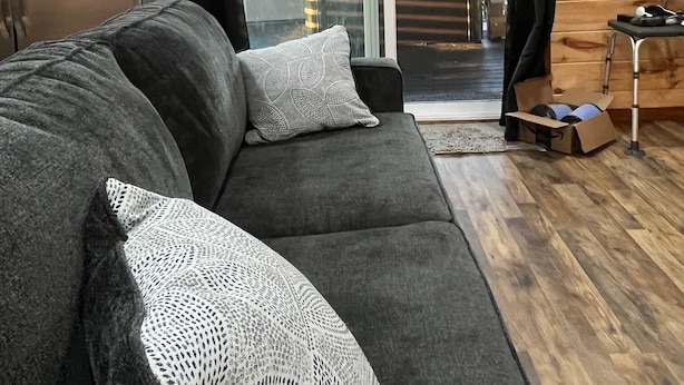 A cozy living area with a grey sofa, a patterned throw pillow, and a wooden floor. A sliding glass door leads to an outdoor patio with a table and chairs.