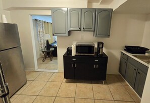 A compact kitchen with grey cabinets, a black countertop, a stainless steel refrigerator, a microwave, and a coffee maker. - Cozy 2-bedroom apartment in awesome East Orange. A place to thrive (East Orange)