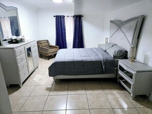 Un dormitorio con cama, cómoda, silla, mesita de noche y espejo.
