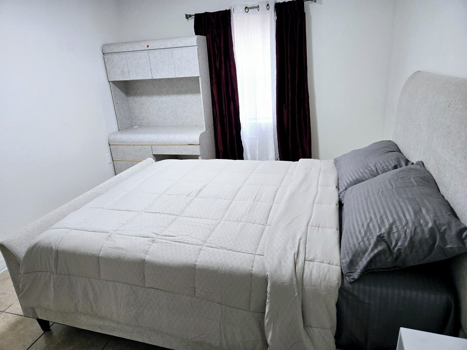 A bedroom with a bed, a nightstand, a wardrobe, and a window with curtains.