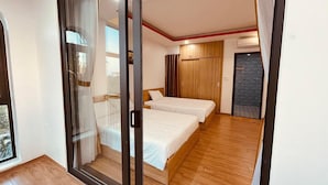 A modern hotel room with a sliding glass door leading to a balcony, a wooden floor, two beds, a wardrobe, and an air conditioning unit. - Hometown An Vien Villa Hoi An (Hoi An)