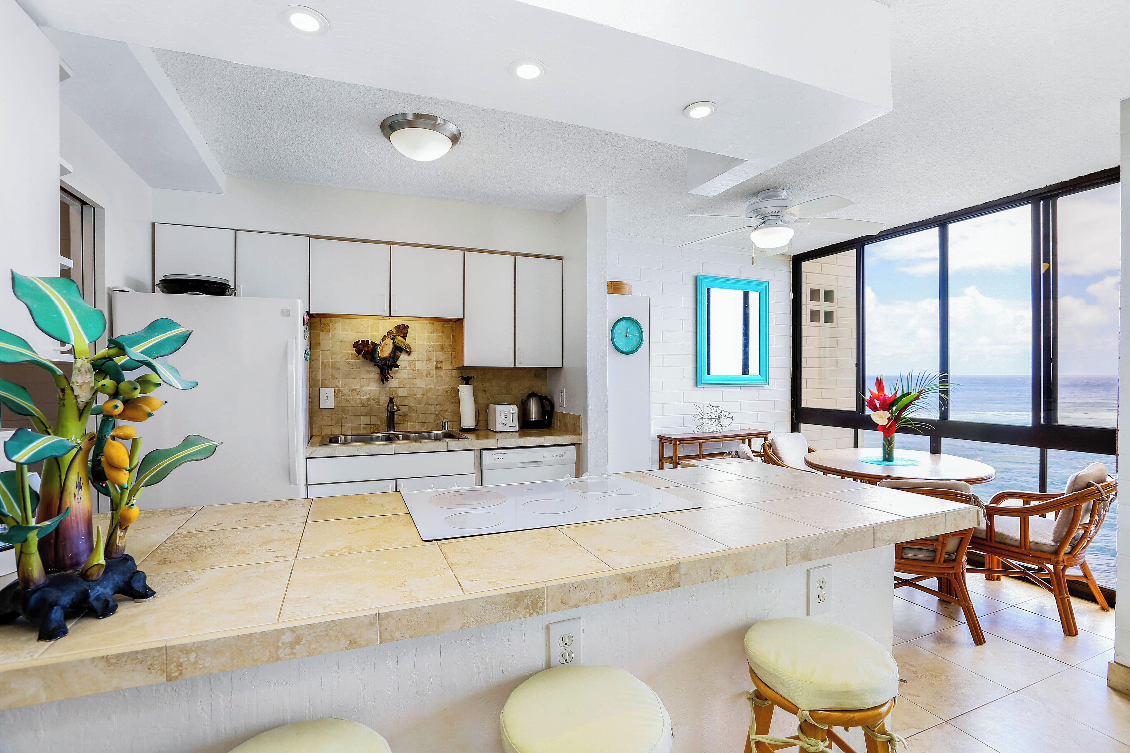 A modern kitchen with a central island, white cabinetry, and a view of the ocean through large windows.