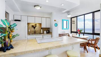 A modern kitchen with a central island, white cabinetry, and a view of the ocean through large windows.
