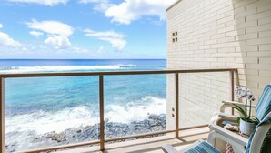 Un balcon donnant sur l’océan, un mur en briques blanches et une chaise sur laquelle est posée une orchidée en pot.