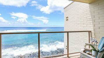A balcony with a view of the ocean, a white brick wall, and a chair with a potted orchid.