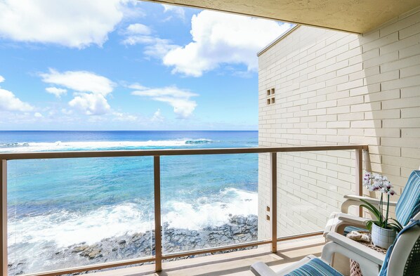 Un balcón con vista al océano, un muro de ladrillo blanco y una silla con una orquídea en maceta.