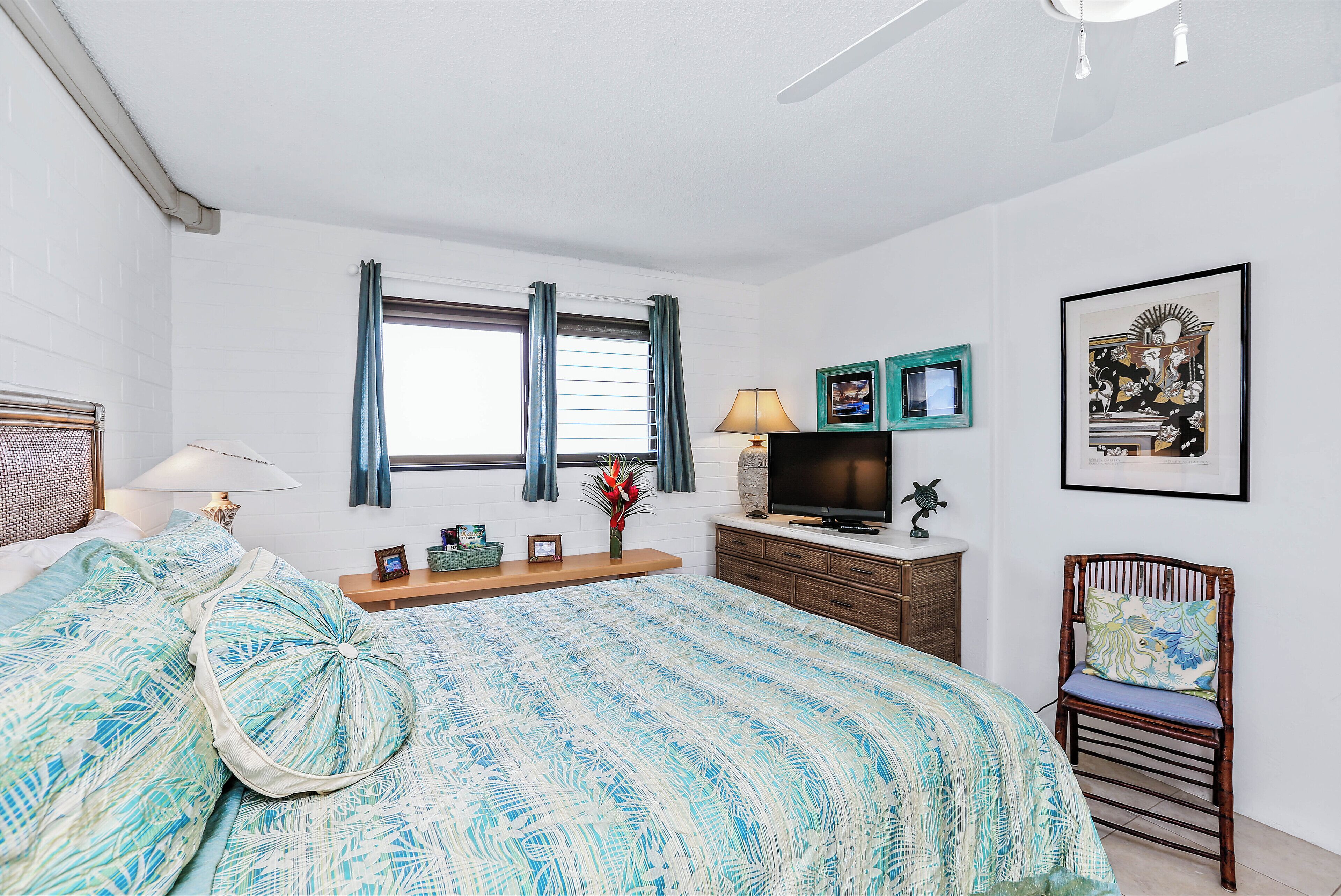A bedroom with a bed, a television, a chair, and a window with curtains.