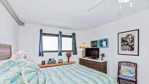 Une chambre à coucher avec un lit, une télévision, une chaise et une fenêtre avec des rideaux.