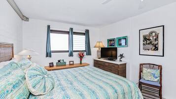 A bedroom with a bed, a television, a chair, and a window with curtains.