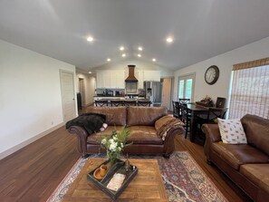 A spacious living room with a brown leather sofa, a dining area with a table and chairs, and a kitchen in the background. - Secluded 2 Story Split Level Home near Wedding Venue Sleeps 2-12 (Huntsville)