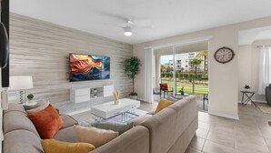 Un salon moderne doté d’un téléviseur à écran plat, d’un canapé, d’une table basse et offrant une vue sur un balcon aménagé avec du mobilier d’extérieur.