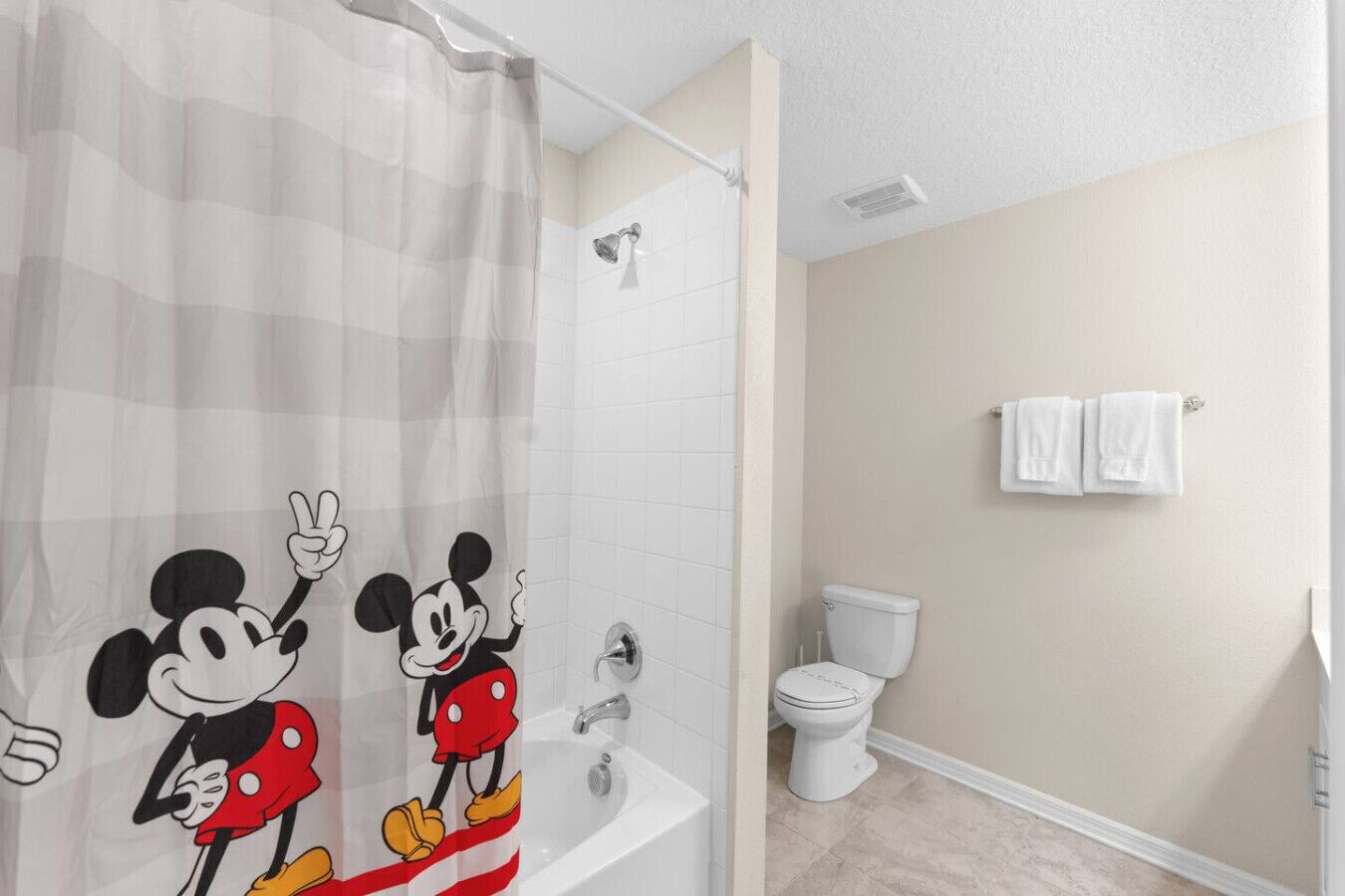 A bathroom with a Mickey Mouse shower curtain, a toilet, and two white towels hanging on the wall.
