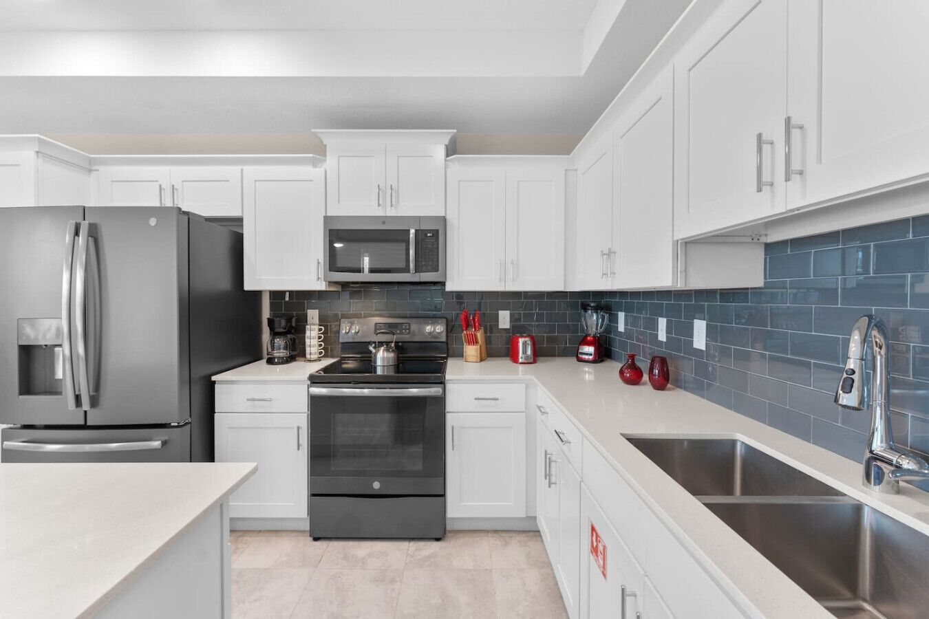 A modern kitchen with white cabinets, stainless steel appliances, and a blue-tiled backsplash.