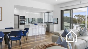 Une cuisine moderne avec des meubles blancs, un îlot central doté de tabourets de bar et un coin repas avec des chaises bleues.
