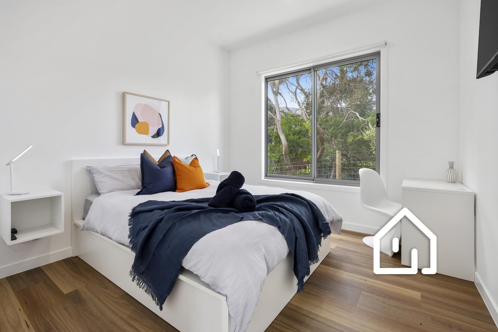 A modern bedroom with a large bed, a bedside table, a chair, and a window with a view of trees.