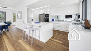 Une cuisine moderne avec des meubles blancs, un îlot central doté de chaises et un coin repas avec des chaises bleues.