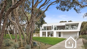 Une maison moderne à deux étages, dotée d’un toit plat, de grandes fenêtres et d’une pelouse bien entretenue.