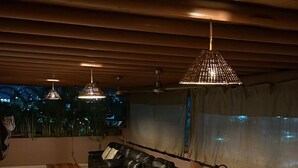 Ein schwach beleuchteter Essbereich mit einem langen Holztisch und Stühlen, Pendelleuchten an der Decke und Blick auf die Stadt durch ein großes Fenster.