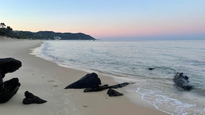 Une plage avec de gros rochers au premier plan, une étendue de sable et une eau calme.