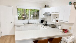 Una cocina moderna con armarios blancos, un lavamanos de acero inoxidable, una estufa a gas y dos taburetes de bar.