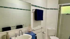 Une salle de bain avec un lavabo blanc, un plan de toilette bleu et un miroir au-dessus. On peut voir des toilettes et une zone douche.