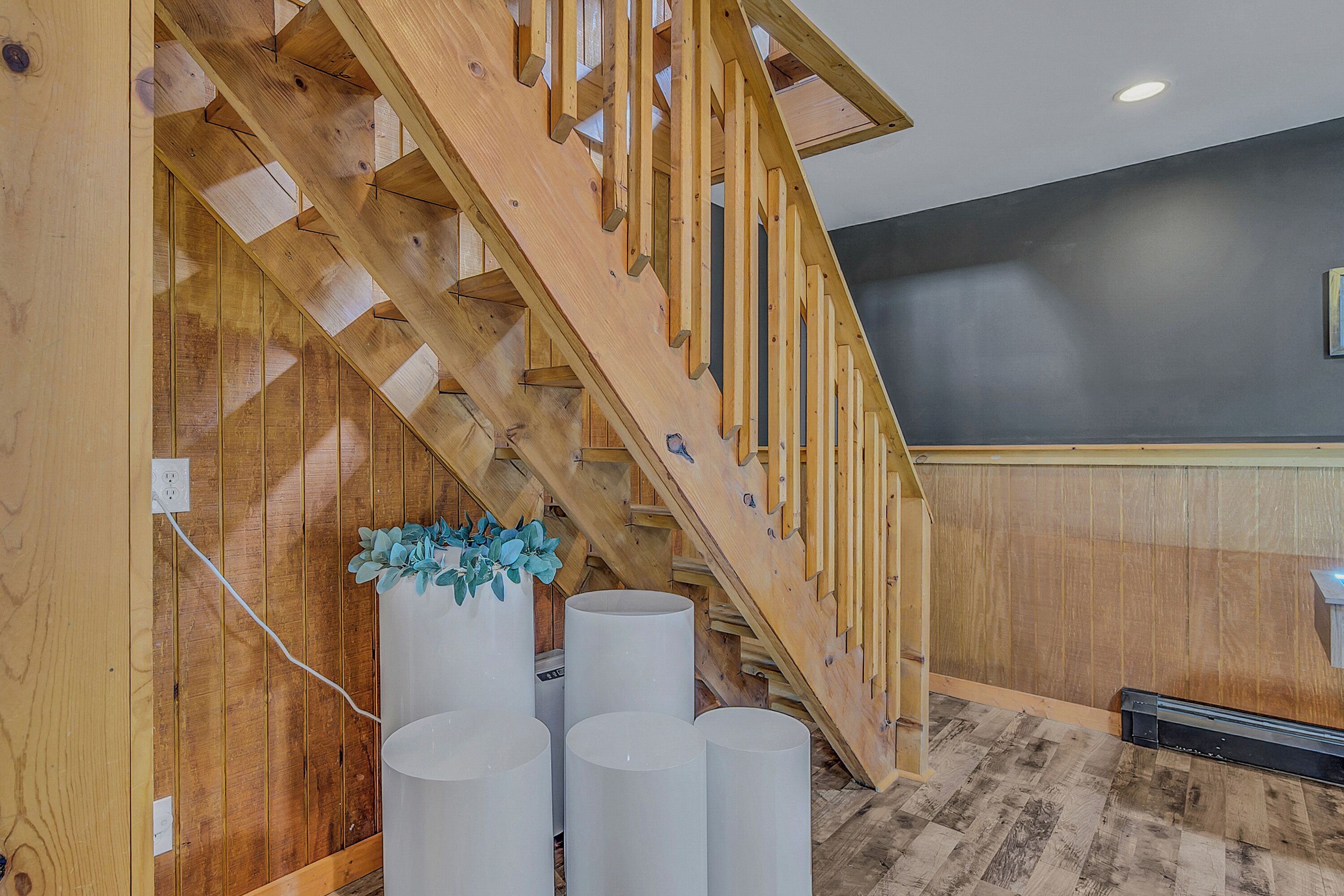 A wooden staircase with a railing, a wall-mounted outlet, and three cylindrical objects on the floor.