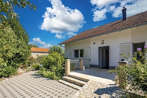 A two-story house with a tiled roof, a paved driveway, and a garden with various plants.