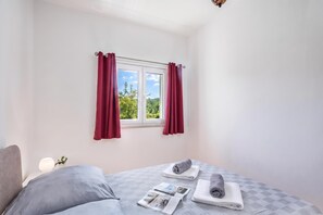 A bedroom with a bed, a window with curtains, and a view of greenery outside.