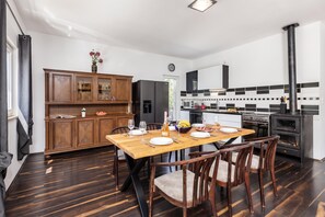 A modern kitchen with a dining area, featuring a wooden cabinet, a refrigerator, a stove, and a dining table set for four. - Holiday Home with Pool near Makarsk, Imotski, Croatia (Imotski)