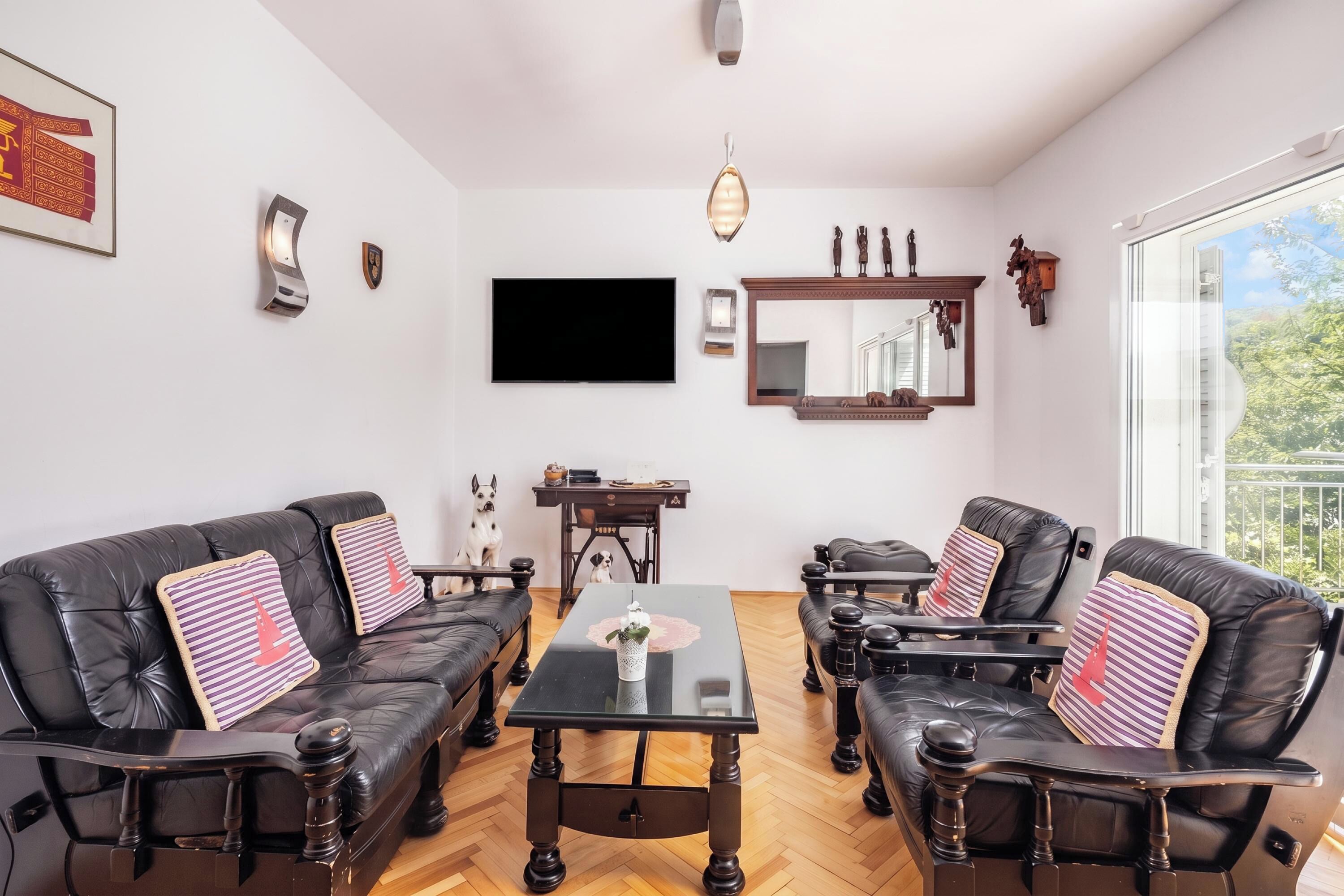 A modern living room with leather sofas, a glass coffee table, and a flat-screen TV mounted on the wall.