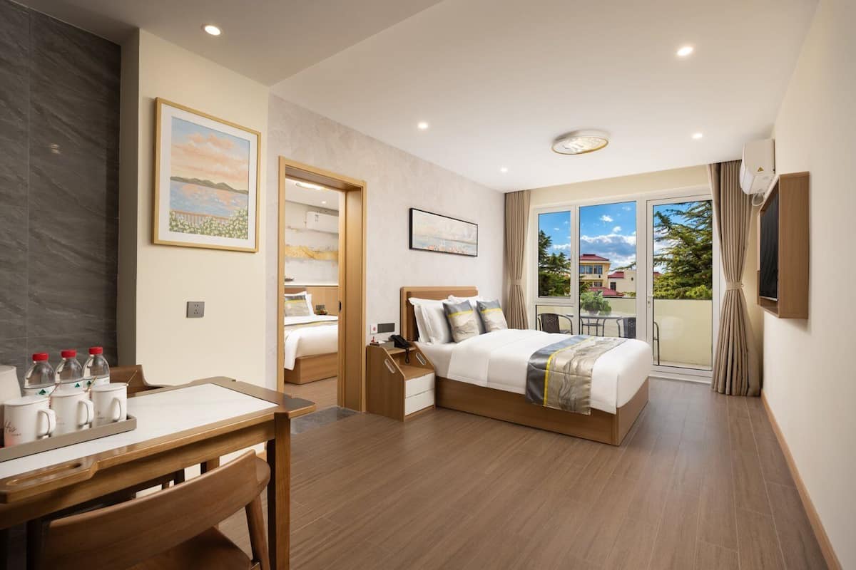 A hotel room with a bed, a desk, a chair, a window with a view, and a door leading to a balcony.