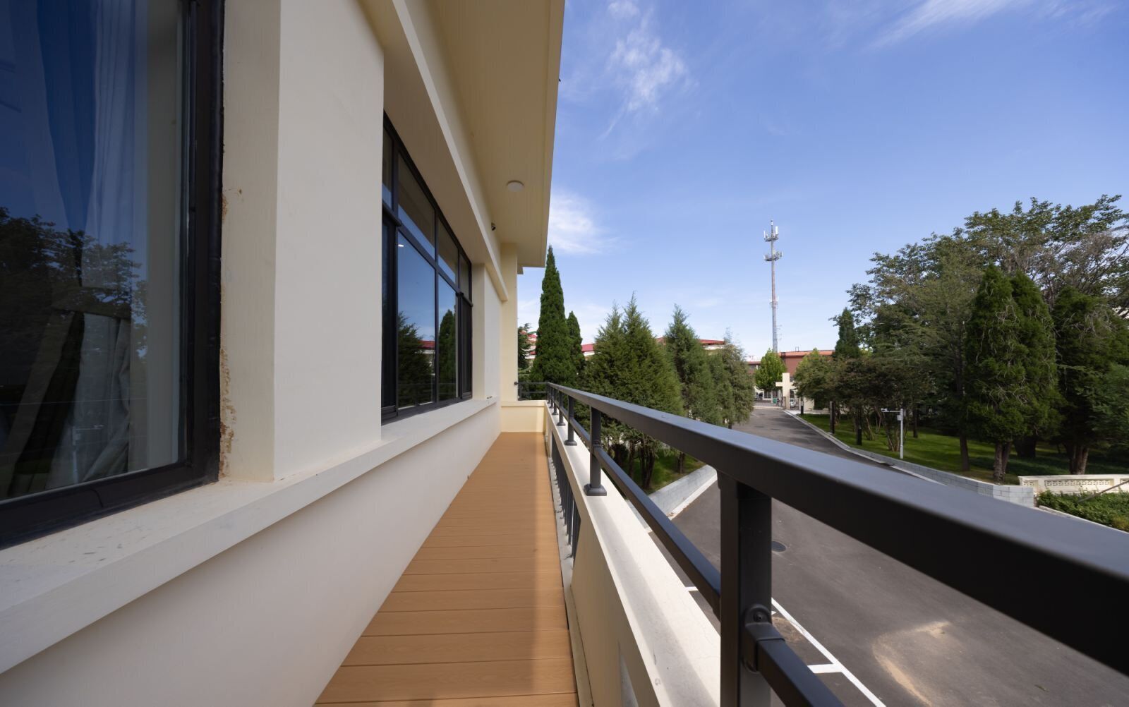 A balcony with a wooden floor, a metal railing, and a view of a street with trees and buildings.