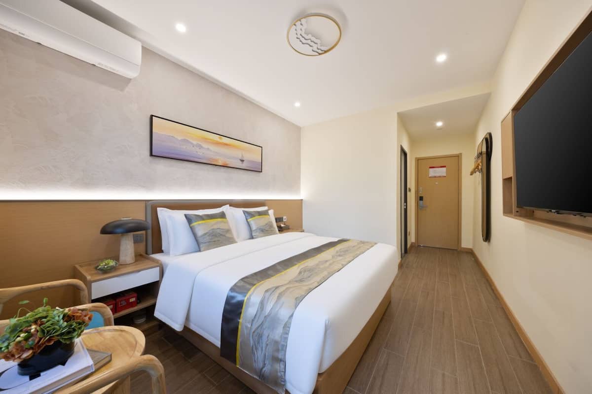 A hotel room with a bed, bedside table, lamp, and a painting on the wall.