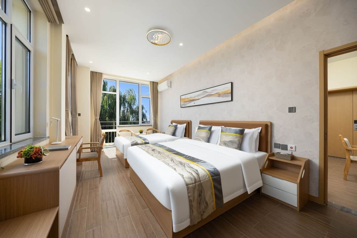 A hotel room with a large bed, a desk, a chair, and a window with a view of trees.