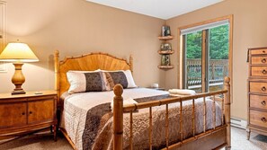 A bedroom with a bed, bedside table, lamp, dresser, and a window with a view of greenery.