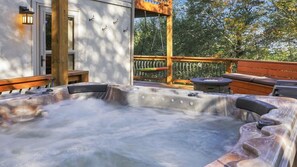 A hot tub with a wooden deck and a stone fire pit.