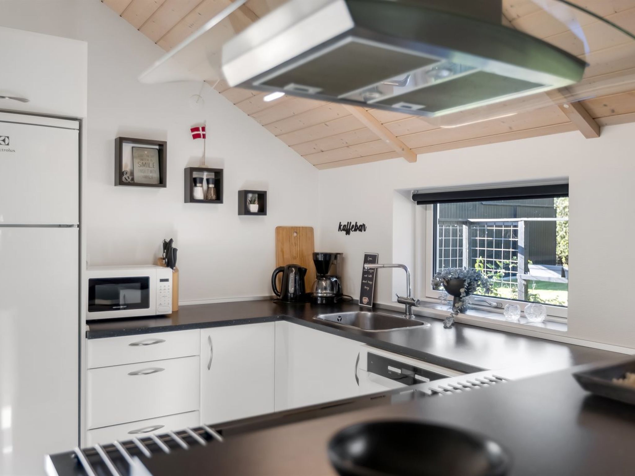 Une cuisine moderne avec des meubles blancs, un four à micro-ondes, une machine à café et une fenêtre donnant sur l’extérieur.