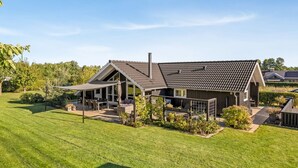 Een modern huis met een groot terras, een overdekte zithoek en een verzorgd gazon.