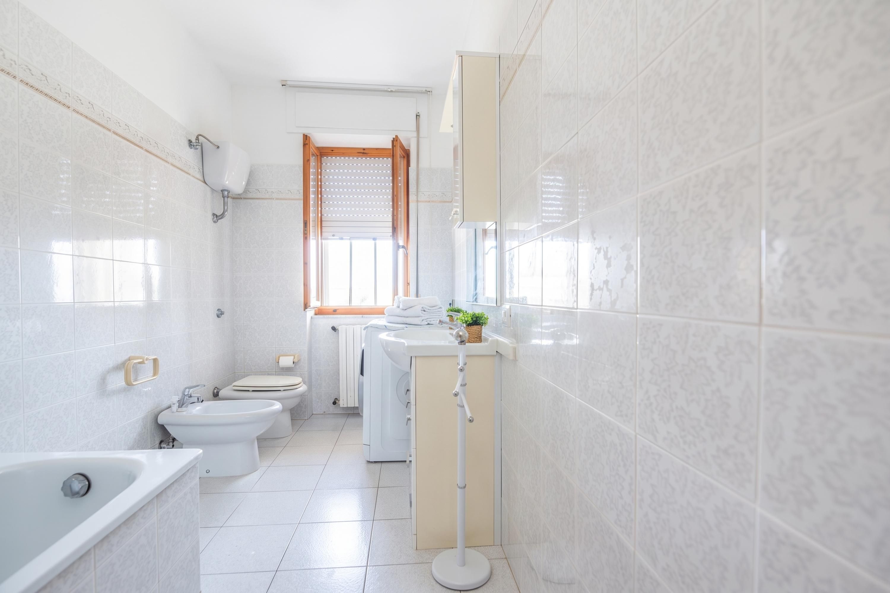 Een kleine badkamer met een bad, een bidet, een toilet en een wasmachine.